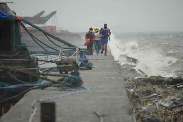 Rescuers run as waves crash on the walkway as they check on residents in a seafront slum in Manila. President Ferdinand Marcos Jr said the evacuation of residents ahead of the storm probably helped save lives. 